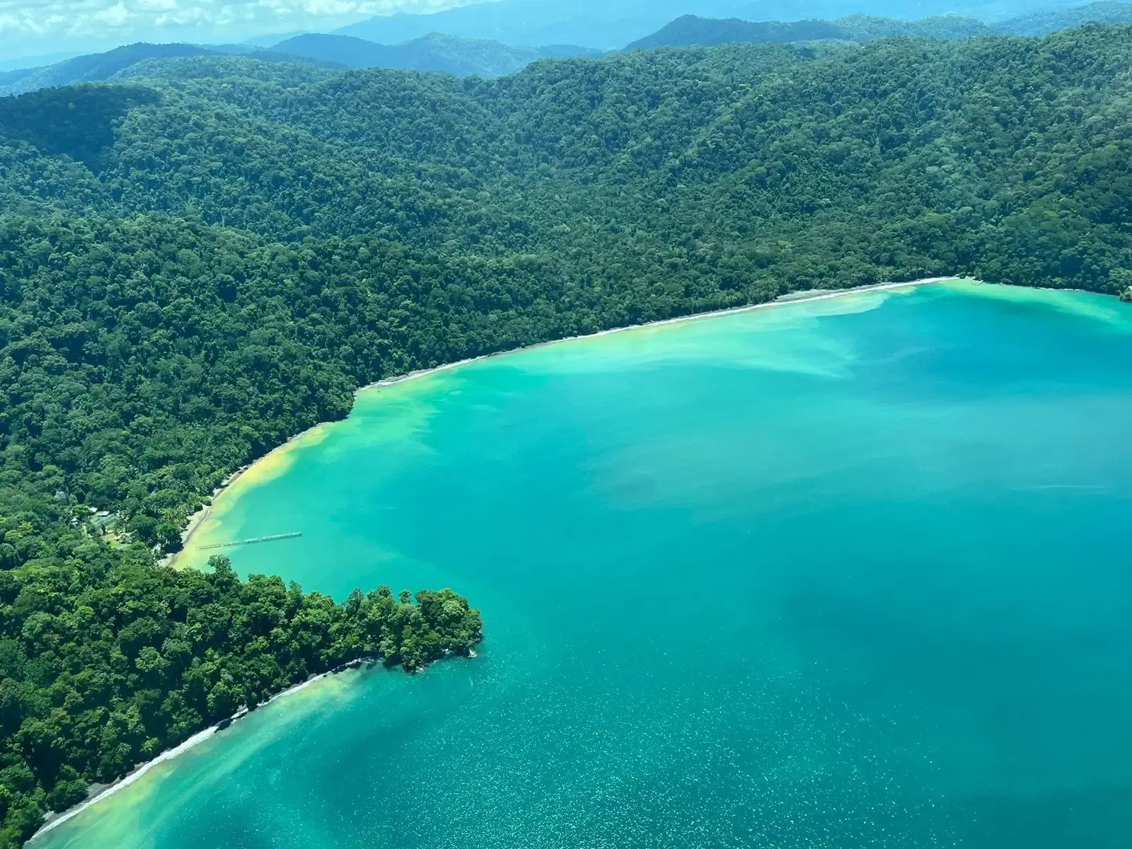 Calm water of the Golfo Dulce at dawn, forested hillsides reflected in the still surface near Pavones