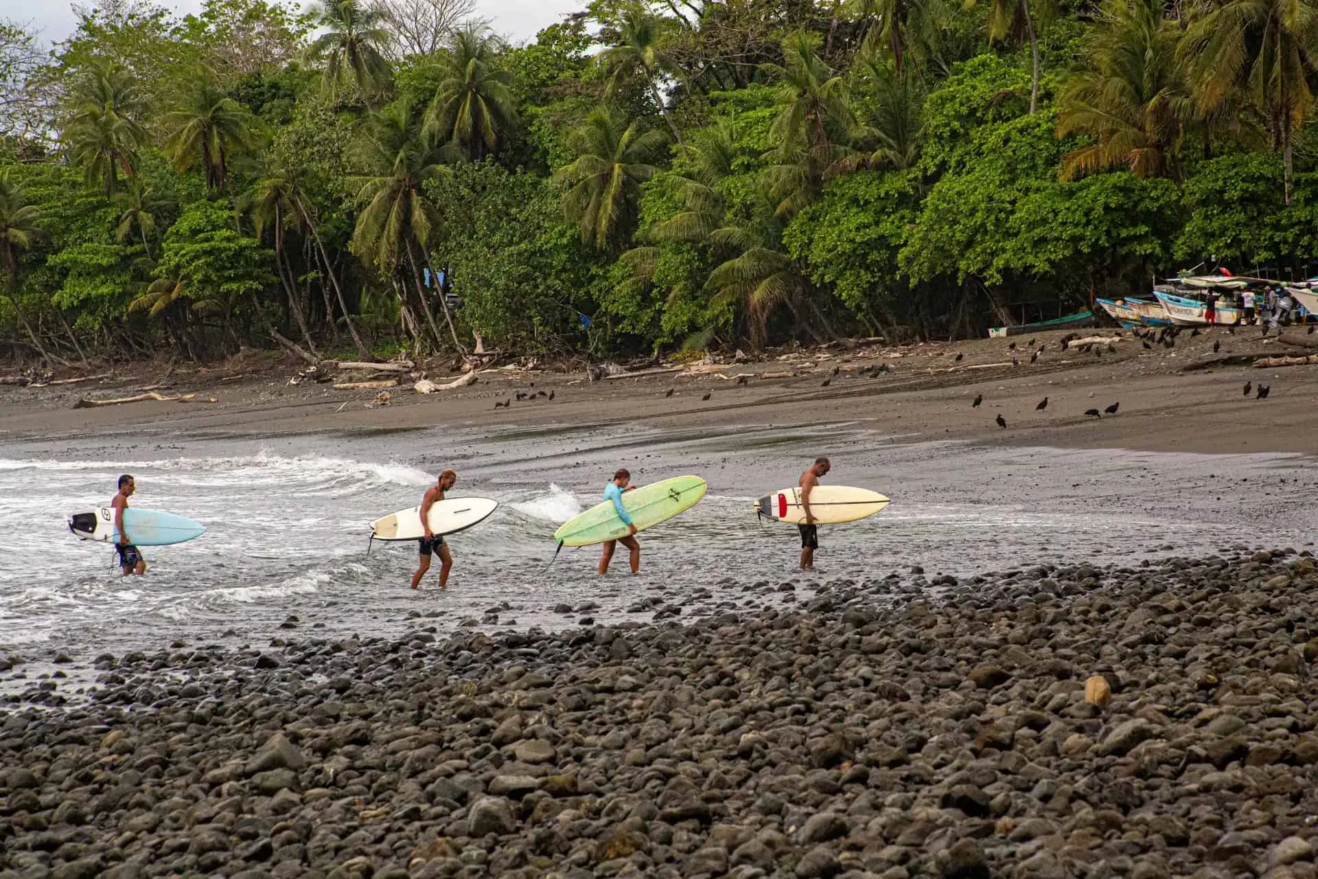 Surfers paddling out through the Pavones shore break, approaching the rocky point on a south swell
